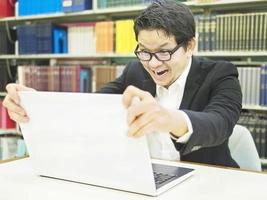 Man is extremely happy when looking some delighted thing on his laptop computer screen in his office. Photo is focused at his face.