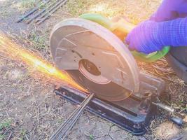 Varilla de acero de corte de la mano del trabajador por una máquina en el sitio de construcción foto