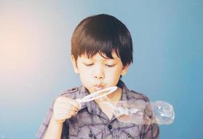 chico asiático está soplando burbujas sobre fondo azul claro foto