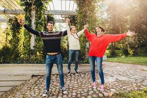 Parents and children concept. Happy family have fun outdoors, female and male play with little kid, swing her in hands, make gestures, have wonderful relationship, enjoy fresh autumn air photo