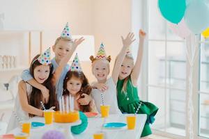 Kids party and celebration concept. Group of small children friends make photo together, raise arms and smile gladfully, have birthday party, festive event, foolish around