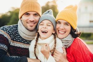 Funny overjoyed small kid laughs as has wonderful time with her parents. Affectionate parents stand near their little daughter who has good mood after spending time on swing. Excitement concept photo