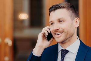 una foto lateral de un apuesto joven habla en roaming a través de un teléfono celular, tiene una expresión positiva, mira cuidadosamente a un lado con espacio para copiar información comercial. concepto de personas y conversaciones