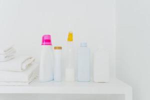 Stack of folded white towels and bottles with detergent against white background. Washing and cleanliness concept. Space for your text photo