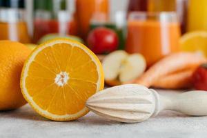 Sliced fresh orange with squeezer. Making juice from fresh fruit. Orange color. Blurred jars of juice in background. Horizontal shot photo