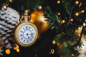 Picture of decorated New Year or Christmas tree with garlands and baubles. Decoration in form of clock symbolizes starting new year. Holidays, celebration, winter concept. photo
