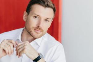 Image of thoughtful self confident male entrepreneur in white shirt, listens attentively his business partner during meeting, poses against white and red background. People, career and lifesyle photo