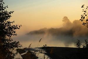 Foggy morning on a European river with fresh green grass in the sun. The rays of the sun through the tree. photo