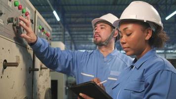 Professional industry engineer teams in hard hats and safety uniforms inspect machine's control panel, maintenance check with tablet in mechanical manufacture factory, electrical service occupation. video