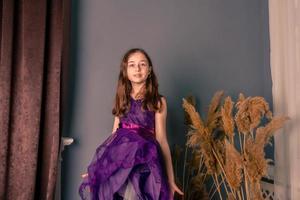 Portrait of a teenage girl in a purple dress in a room. The girl on the background of a gray wall. photo