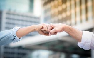 Two roll up shirt sleeves businessman making a first bump complete deal with blurred building background, successful business collaboration and teamwork,Team agreement in hands gesture communication photo