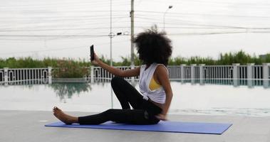 een vrouw gekleed voor oefening zit op een yogamat pratende smartphone video-oproep. video