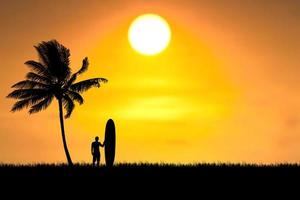 los surfistas de silueta escuchan en la playa con cocoteros por la mañana. foto