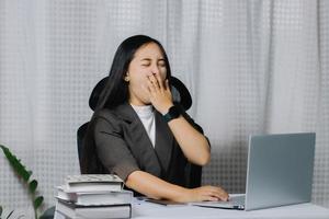 mujer asiática bostezando mientras trabaja en una laptop en su oficina. foto