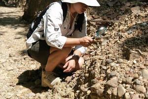 investigadora geóloga asiática analizando rocas con una lupa en el parque natural mae wang, tailandia. geólogo de exploración en el campo
