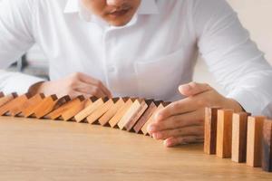 Risk management and business strategy concept, businessman hands stop the dominoes from falling continuously, preventing future risks from crisis. photo