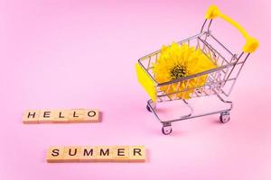 Hola Verano. carrito de compras con flores. flor amarilla sobre fondo rosa. foto