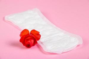 toalla sanitaria y flor roja sobre fondo rosa. concepto de menstruación. foto
