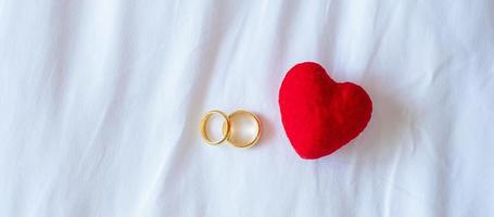 decoración en forma de corazón y anillo de compromiso de pareja dorado sobre fondo blanco. concepto de amor, juntos y feliz día de san valentín foto