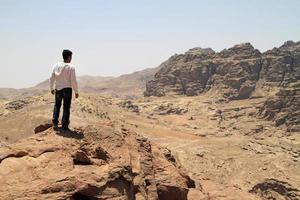 Young man on top of a peak looking over a valley in the rugged landscape of Petra, Jordan photo