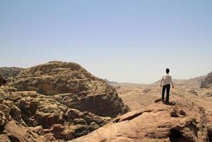 joven en la cima de un pico con vistas a un valle en el accidentado paisaje de petra, jordania foto