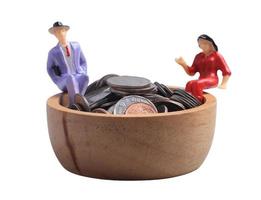 Miniature people. Standing on a wooden bowl with coins on a white background. Money saving concept. photo