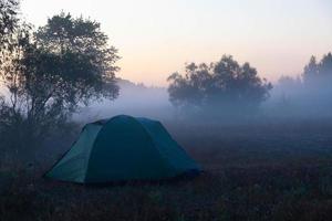 carpa turística verde junto al río al amanecer, con niebla matutina de otoño en el agua. paisaje turístico al aire libre. foto