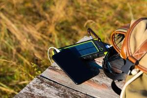 Solar energy battery device, power bank and telephone on a wooden table with a backpack. Solar charge your smartphone. Selective focus photo