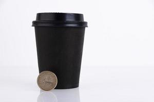 vaso de plástico negro cerrado para café o té con una moneda de un dólar, sobre un fondo blanco. copie el espacio foto