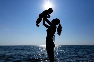 una niña sostiene a un niño en sus brazos contra el sol. fotografía de silueta. foto