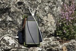 The smartphone is charged with a portable solar power bank charger on a rock during extreme travel. photo