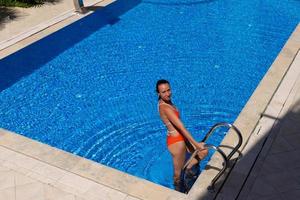 una bella, joven y bonita morena con traje de baño rojo se relaja en una piscina con agua azul. foto