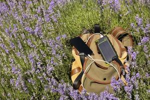 el teléfono inteligente se carga con un banco de energía de cargador portátil en un panel solar, en el fondo de una mochila mientras viaja foto