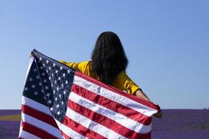 una mujer joven de cabello oscuro que sostiene la bandera de los estados unidos de américa contra el cielo soleado. día conmemorativo y concepto del día de la independencia de estados unidos. foto