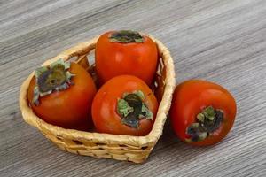 Persimmon in a basket on wooden background photo