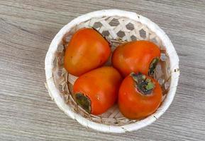 Persimmon in a basket on wooden background photo