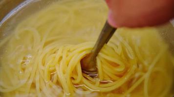 gros plan sur une main soulevant des pâtes spaghetti cuites à la vapeur bouillies avec des pinces. cuisiner à la maison. préparation pour faire des spaghettis carbonara maison. video