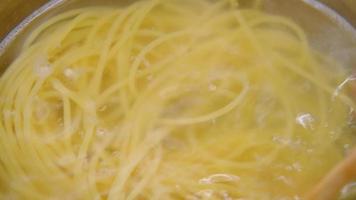 en remuant à la main des pâtes spaghetti bouillies dans une casserole sur la cuisinière avec une louche en bois. cuisiner à la maison. préparation pour faire des spaghettis carbonara maison. video