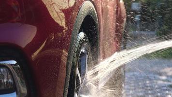 close-up van water dat op een auto stroomt terwijl een werknemer een hogedrukreiniger gebruikt om de auto te wassen. carwash serviceconcept. video