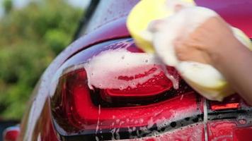 Close-up of a woman's hand washing a car with sponge and soap on the car wash. Manual car wash with white soap. Car wash service concept.