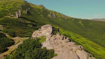 Hiker stands on a rock, looking to the future at sunset. A male athlete stands on top of a mountain, looking into the distance. Aerial view in a circle video