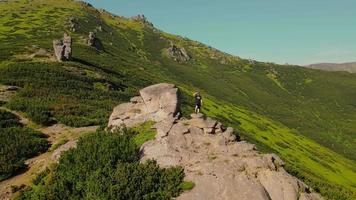 excursionista se encuentra en una roca, mirando hacia el futuro al atardecer. un atleta masculino se para en la cima de una montaña, mirando a lo lejos. vista aerea en un circulo video