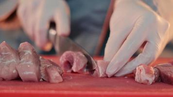 cortar carne cruda con un cuchillo de cerca. el chef corta el cerdo en trozos para cocinar a distancia. video