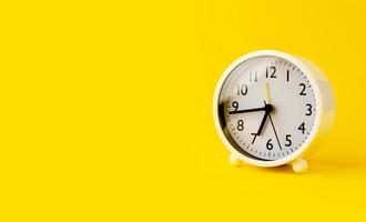 White alarm clock telling the time set on a yellow background. concept of the importance of time photo