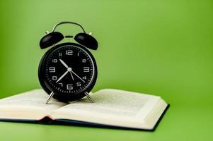 black clock It's on a thick book, open and ready to read. on a green background The concept of learning education with open books or textbooks, stacks of literature, texts, academic documents. photo