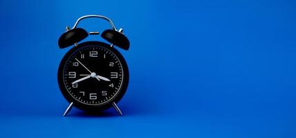 despertador negro sobre fondo azul, importancia del concepto de tiempo y trabajo del tiempo. foto