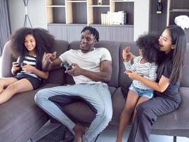 Family mother father son girl boy black African person daughter kid young play video game joystick console controller technology entertainment indoor room house sitting sofa lifestyle funny enjoy cute photo