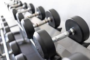 pararse con pesas. Sala de deportes y fitness. equipo de entrenamiento con pesas. juego de mancuernas negras, muchas mancuernas en el rack en el gimnasio deportivo foto