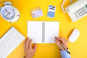 Office desk with smartphone, laptop computer, cup of coffee, and office tools. Flat lay, top view with copy space. A bank notepad and a pen are on top of an office desk table containing computer tools photo