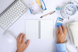 Office desk with smartphone, laptop computer, cup of coffee, and office tools. Flat lay, top view with copy space. A bank notepad and a pen are on top of an office desk table containing computer tools photo